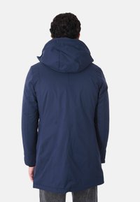 Parka impermeabile blu navy con cappuccio, caratterizzata da un esterno liscio e maniche lunghe, che arriva a metà coscia vista da dietro.