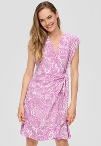 Wikkeljurk van lichtroze stof met witte bloemenpatronen, korte mouwen en een knoopdetail in de taille, wat een vloeiende silhoutte creëert.