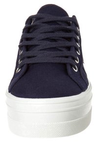 Námořnické plátěné tenisky s bílou gumovou podrážkou, kulatou špičkou a plochými tkaničkami. Obsahují kovové očka a texturovaný povrch látky.