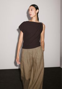 Tmavě hnědý top s krátkým rukávem a lodičkovým výstřihem, se stříbrným detailem. Spárován s volnými, světle hnědými, skládacími kalhotami.