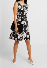 Květinové bezramenné šaty v černé barvě s růžovými a zelenými květy. A-liniová silueta, doplněná černou kabelkou a bílými podpatky.