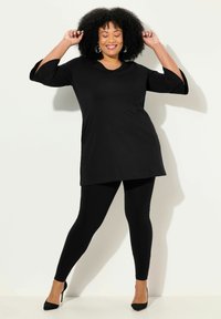 Tunic nera con maniche a tre quarti, abbinata a leggings neri e tacchi alti neri. Tessuto morbido, design semplice senza fantasie o accentuazioni.