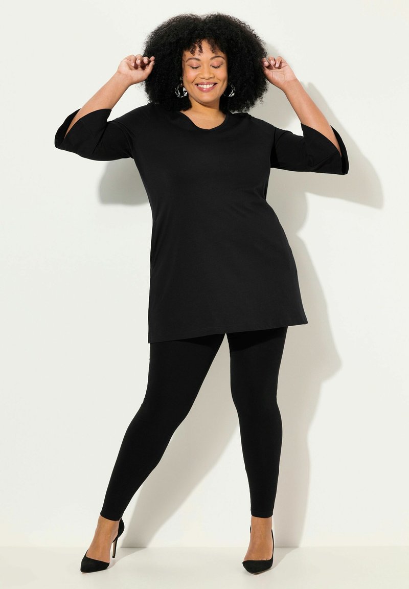 Tunic nera con maniche a tre quarti, abbinata a leggings neri e tacchi alti neri. Tessuto morbido, design semplice senza fantasie o accentuazioni.