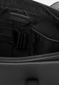 Schwarze Handtasche aus Kunstleder mit einem Innenfutter, das einen Reißverschluss, mehrere Kartenfächer und ein markiertes Patch sowie ein glattes Textilfutter bietet.