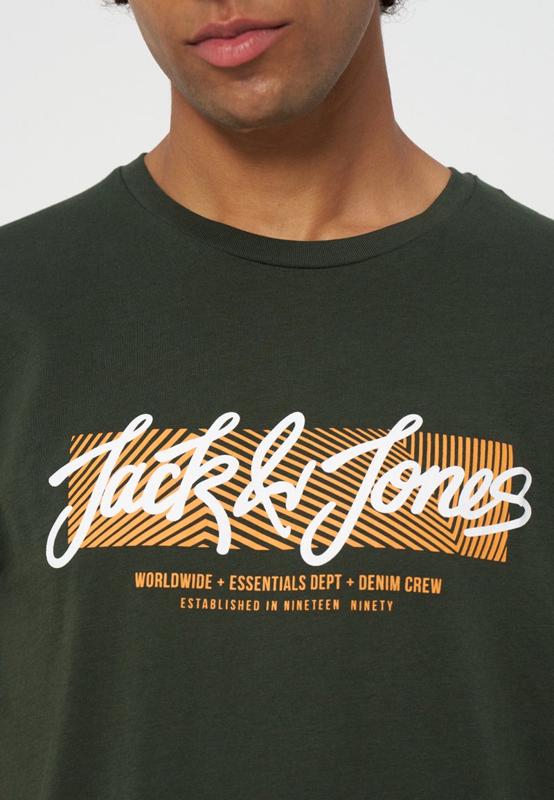 Persona que lleva una camiseta verde oscuro con texto "Jack & Jones" en naranja y blanco y un diseño a rayas en el pecho.