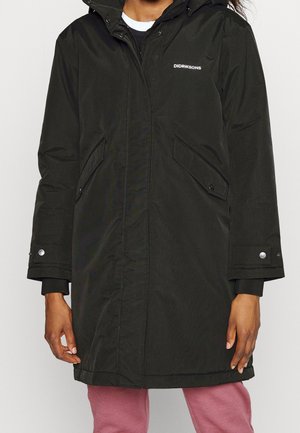 Personne portant un parka noir Didriksons à capuche avec des poignets boutonnés et des poches avant inclinées, associé à un pantalon rose.