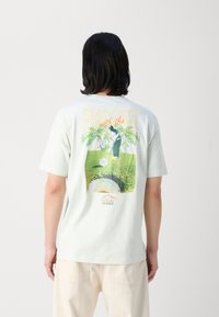 Ljusgrön t-shirt med kort ärm och tryckt grafik av en golfspelare samt texten "SMOOTH with the ROUN". Mjuk textur, avslappnad passform.