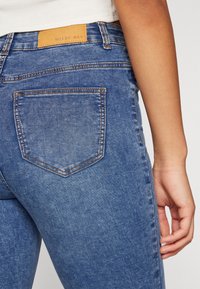 Blå denimjeans med medelhög midja, utrustade med en lädermärke, subtil sömnad och två bakfickor. Slät textur, klassisk passform.