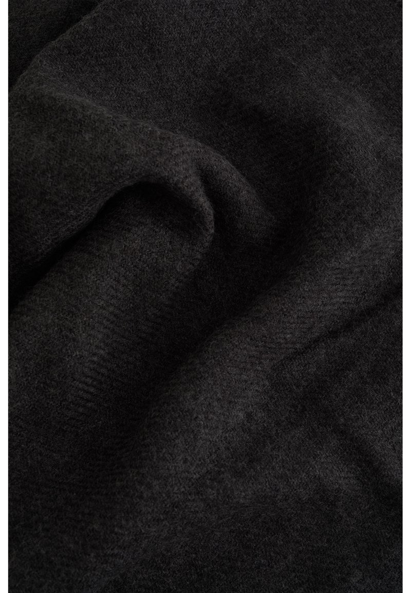 Tumši pelēks audums ar mīkstu, teksturētu virsmu un smalku zivs kaula rakstu, nolikts un nedaudz krunkains, parādot materiāla dziļumu.