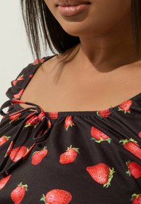 Czarna bluzka z tkaniny z nadrukiem truskawek, z okrągłym dekoltem i marszczonymi rękawami. Szczegół ze sznurkiem przy dekolcie dodaje faktury.