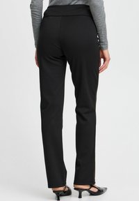 Black stretchy pants with a thick waistband, slim fit, and smooth texture. Designed with a full length and minimal detailing.