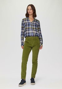 Gestreepte button-up shirt in marineblauw, groen en wit; gecombineerd met olijfgroene corduroy broek. Model draagt donkere sneakers met een lichte zool.