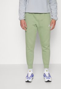 Lys grønne bomullsjoggers med elastisk midje og sidelommer, kombinert med hvite og blå joggesko. Grå fleecegenser.