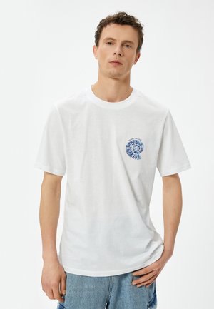 Hvid bomulds t-shirt med korte ærmer, der har et farverigt spiral grafisk design på venstre brystområde. Casual pasform, rund halsudskæring.