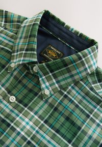 Green and blue plaid button-up shirt, cotton fabric, collar with white buttons, and a navy inner lining with a branded tag.