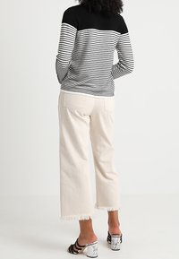 Sweter w paski z czarnymi naramkami i pionowymi paskami w białym i czarnym kolorze; zestawiony z kremowymi spodniami o szerokich nogawkach z postrzępionymi brzegami i marmurowymi obcasami.