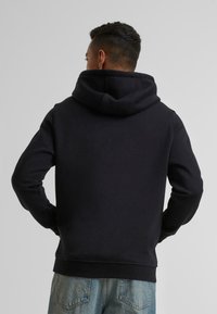 Zwarte hoodie met een grote capuchon, geribde manchetten en onderkant, en een eenvoudig vlak achterontwerp, gecombineerd met lichtblauwe spijkerbroek.