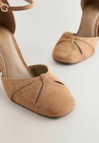 Beige Wildleder-Peeptoe-Schuhe mit strukturierter Oberfläche, einem gekreuzten Riemendesign, einem Knöchelriemen mit Schnalle und einem Blockabsatz.