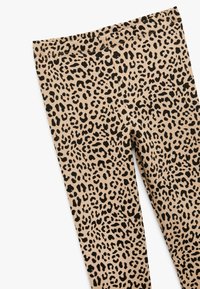 Lepardprint leggings lavet af strækbart stof, med en tan base og sorte pletter, elastisk talje, glat tekstur og tætsiddende design.