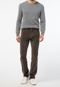 Grå stickad tröja, bruna kordfläskbyxor och vita sneakers. Tröjan har en rund midja, medan byxorna har framfickor och bältesöglor.