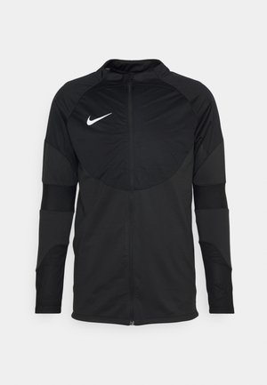 Zwarte Nike-jas met ritssluiting, lange mouwen en een ronde schouderontwerp. Kenmerkt textuurelementen op de mouwen en een wit logo op de borst.