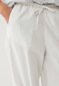 Pantaloni leggeri in lino bianco con cintura elastica e cordoncino. Presentano tasche laterali e una superficie liscia, leggermente texturizzata.