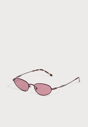 Lunettes de soleil ovales aux verres teintés rose, avec une fine monture en métal sombre et des plaquettes de nez transparentes, sur un fond clair uni.