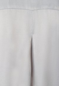 Hellgraue Hose aus glattem Stoff, mit einer mittigen Naht auf der Rückseite und einem dezenten Schlitzdetail am Saum. Einfarbige Textur mit minimalen Akzenten.