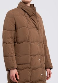Brown quilted outerwear featuring a high collar, snap buttons, and a textured surface with a soft finish. Focus on warmth and comfort.