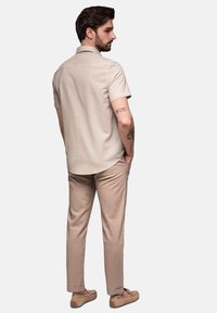 Korte mouwen beige shirt met een ronde zoom, gecombineerd met licht beige broeken. De outfit heeft gladde texturen en subtiele tailledetails.