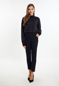 Pulover marin cu puncte aurii, mâneci lungi și decolteu rotund, combinat cu pantaloni negri ajustați și pantofi cu toc negru.
