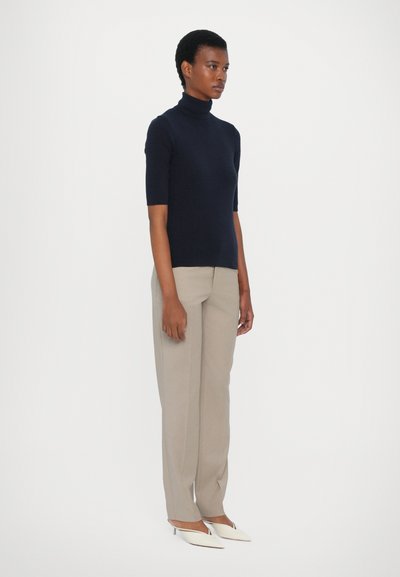Jūras spēku turtleneck krekls ar īsām piedurknēm, savienots ar bežām platas kājas biksēm un baltām norādītā pirksta kurpēm. Gluda auduma, minimāla dizaina.