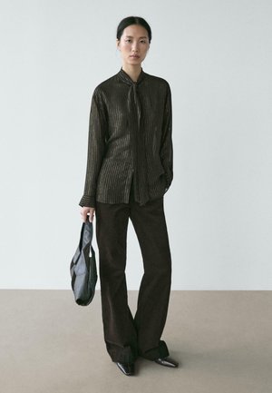 Camicia nera a righe metalliche con bottoni e colletto a cravatta, abbinata a pantaloni marrone scuro a gamba larga e una borsa nera a tracolla. Scarpe nere a punta.