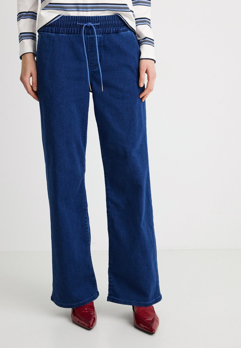 Pantalones de mezclilla de pierna ancha en azul profundo con cintura elástica y cordón. La tela parece suave con una textura lisa.