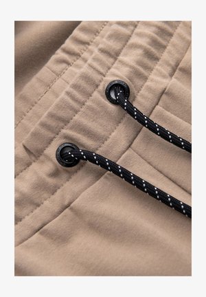 Tejido beige con una textura suave; presenta cordones negros con acentos blancos y herrajes de plástico. Diseñado para un ajuste ajustable.