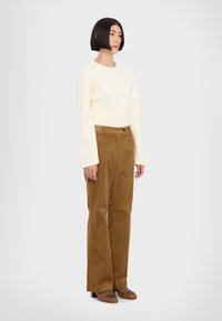 Pulover crem cu fir texturat, cu mâneci lungi, asortat cu pantaloni drepți din catifea la o culoare maro și mocasini maro cu un detaliu închis.