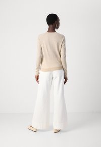 Beige stickad tröja med långa ärmar, avslappnad passform, ribbade mudd, i kombination med vida vita byxor och ljusbeiga slip-on skor.