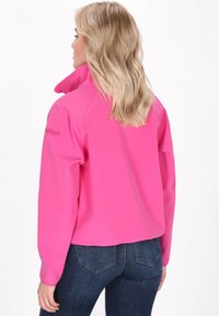 Fuksijos spalvos megztinis su aukšta apykakle, ilgomis rankovėmis ir lygiu paviršiumi; derinamas su tamsiai mėlynomis džinsomis. Matomas prekės ženklas ant peties.