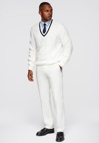 Maglione bianco a trecce con scollatura a V, camicia dress leggera blu, pantaloni bianchi su misura e scarpe nere con nappine. Design semplice, texture liscia.