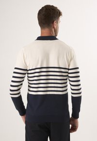 Gestreifter Pullover in Marineblau und Creme, mit einem Polo-Kragen, gerippten Bündchen und Saum, der horizontale Streifen im oberen und unteren Bereich aufweist.