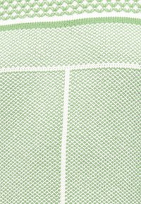 Tissu en tricot vert et blanc avec des lignes blanches verticales et horizontales formant un motif en grille.