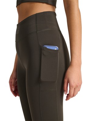 Nahaufnahme einer Person, die schwarze Leggings mit hohem Bund und einer Seitentasche trägt, in der ein blaues Smartphone steckt, Hand locker seitlich hängend.