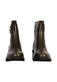 Stivali alla caviglia in pelle marrone con punta arrotondata, tacco robusto, chiusura con zip e una fascia decorativa con un accento dorato circolare.