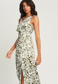 Maxi dress in white and green floral pattern, featuring a wrap design, deep V-neck, and thigh-high slit, crafted from lightweight fabric.