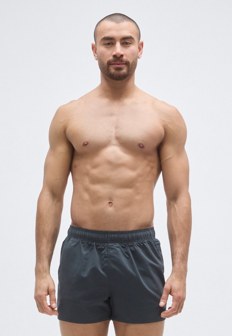 Γκρι μαγιό βερμούδα με ελαστική μέση, ομαλή υφή και εφαρμοστή σχεδίαση. Απλό χρώμα χωρίς σχέδια ή επιπλέον διακοσμήσεις.