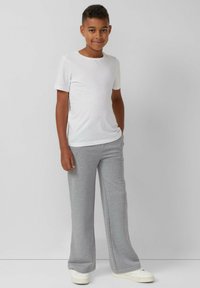 Witte t-shirt met korte mouwen en lichtgrijze joggingbroek, met een losse pasvorm. De broek heeft een elastische tailleband en een subtiele textuur. Witte sneakers.