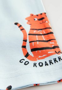 Lyseblåt stof med et legesygt orange stribet tigermotiv med sorte konturer. Teksten nedenfor lyder "GO ROARRRR" med fede sorte bogstaver.
