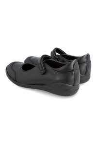 Zapatos de cuero negro con puntera redondeada, correa ajustable y panel lateral texturizado. Suela de perfil bajo con un sutil logotipo cerca del talón.