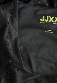Haut de sport noir avec une texture à pois, doté de petits accents brillants. Logo et étiquette de taille en vert vif, situés sur le côté intérieur.
