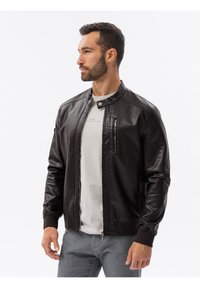 Giacca di pelle nera con colletto alto, zip frontale e tasche laterali. Presenta polsini a costine e una texture liscia.